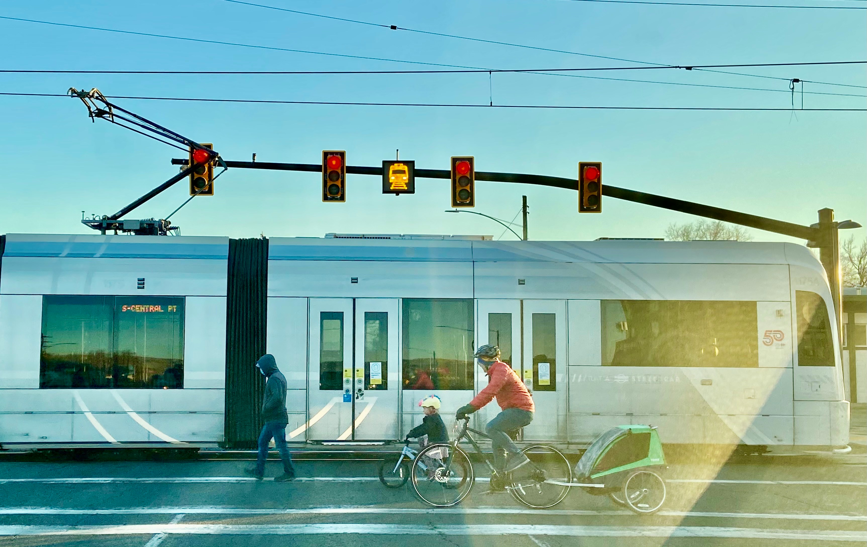 Two people and a child cross a street in front of a tram.