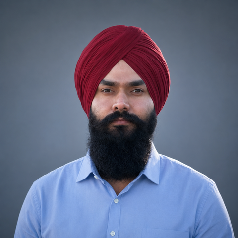 A man with a beard and a red turban looks at the camera.