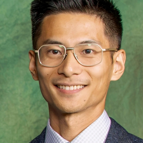 Headshot of a man in a suit and tie with glasses smiling at the camera.